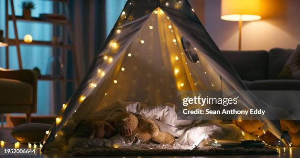 child, fort and sleeping with blanket in a family home at night with sleepover, nap and rest. lights, teddy and young girl in a lounge with kid, teepee and evening in a living room in a house - sleepover bildbanksfoton och bilder