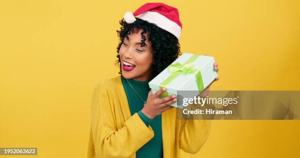 woman, christmas and gift box for festive season or december giving on a yellow studio background. young female person holding present with hat for giveaway, fashion or celebration on mockup space - giveaway stock pictures, royalty-free photos & images