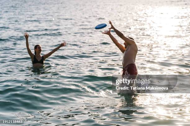 man and woman plays with frisbee in the sea on sunset light. beach holidays. - throwing frisbee stock pictures, royalty-free photos & images