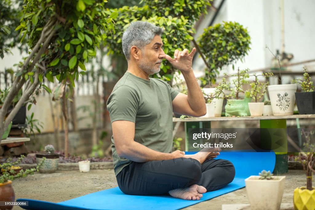 Old man meditating on exercise mat in park