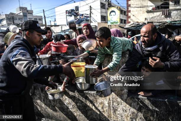 Palestinian people reach out for food with empty containers as food is distributed by charitable organizations while Israeli attacks continue in...