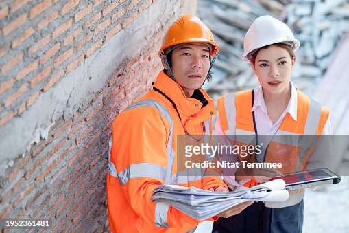 Enhanced Project Planning and Scheduling with Construction Project Management Solution. A male Japanese construction engineer and female project manager examine and discuss the construction work phase at a construction site.