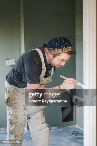 Young, skilled Painter & Decorator overcoming the disability of having one hand as he carefully and skilfully paints a door architrave in a residential house