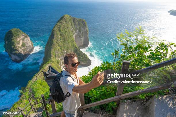 junger mann macht selfie am strand von kelingking von oben. - nusa penida stock-fotos und bilder