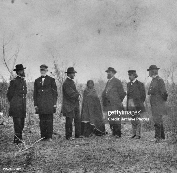 Members of the Peace Commission pose on either side of a Native American woman, wrapped in a blanket, during negotiations for the Treaty of Fort...