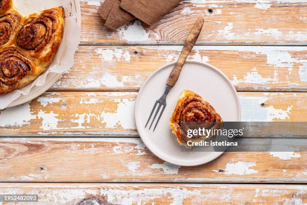 freshly baked cinnamon bun on plate on rustic wooden table - sticky bun stock pictures, royalty-free photos & images