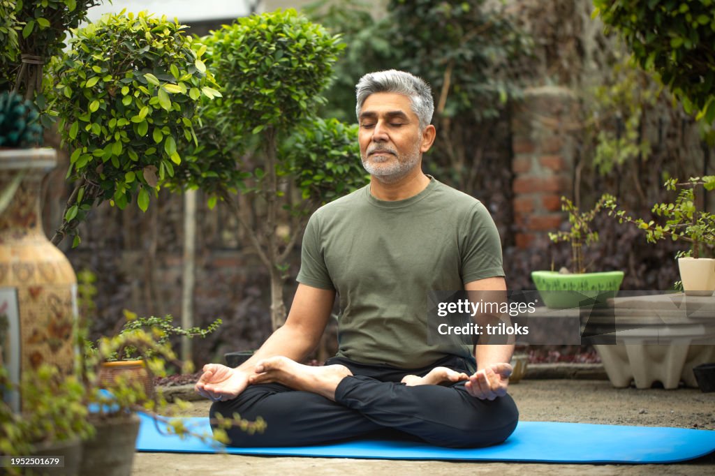 Old man meditating on yoga mat in yard