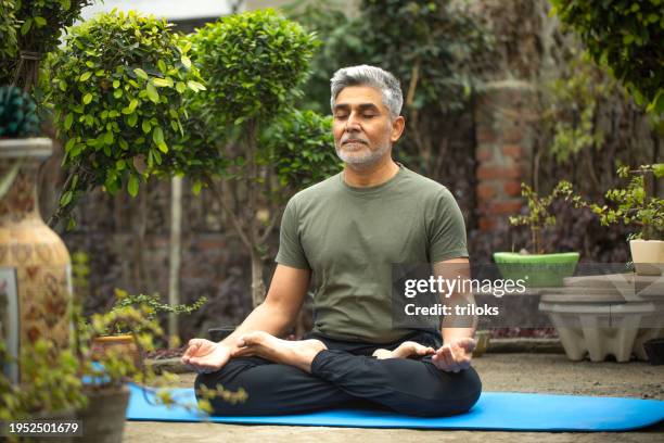 old man meditating on yoga mat in yard - budismo imagens e fotografias de stock