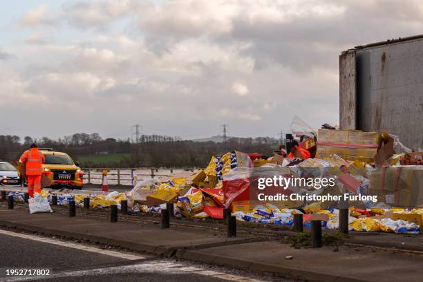 Workers clear up Wotsits and Quavers savoury snacks from the M6 motorway northbound after the wind overturned lorries on the carriageway on January...