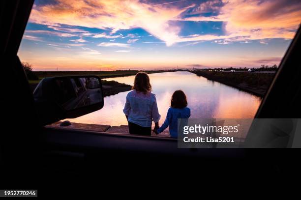 girls on a road trip with car looking at a beautiful sunset on pit stop during vacation - wonderlust stock-fotos und bilder