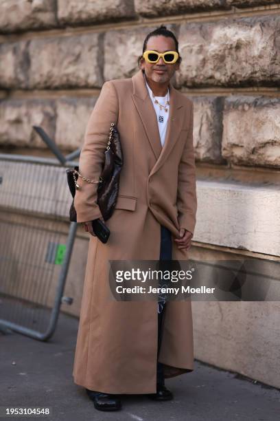 Fashion Week Guest is seen wearing a brown long coat, white Loewe shirt, denim blue Loewe jeans, yellow sunglasses and a brown Loewe handbag and a...