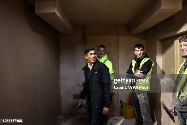 Britain's Prime Minister Rishi Sunak talks with trainees as he plasters a wall during a visit of the Construction Skills Village on January 25, 2024...