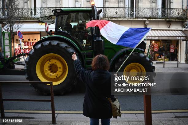 Woman waves a French flag past a tractor as farmers take part in a nation-wide day of actions and road blockades called by several farming unions to...