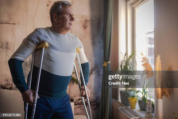 an elderly man walks with the help of crutches - crutch stock pictures, royalty-free photos & images