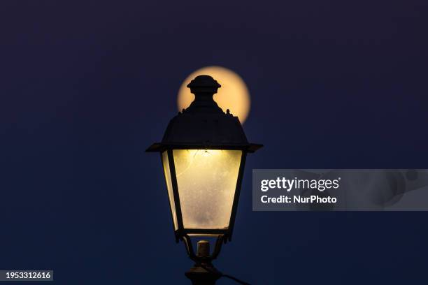 The Full Wolf Moon rises beside a street lamp on January 25 in San Cataldo, Italy. This lunar event, known as the Wolf Moon, receives its name from...