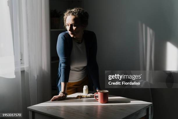 a woman standing at a table with yellow and green pills in her hand - hot flash stock pictures, royalty-free photos & images