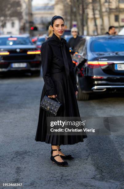 Bettina Looney wears black bag, pleated skirt, blouse, heels outside Dior during the Haute Couture Spring/Summer 2024 as part of Paris Fashion Week...