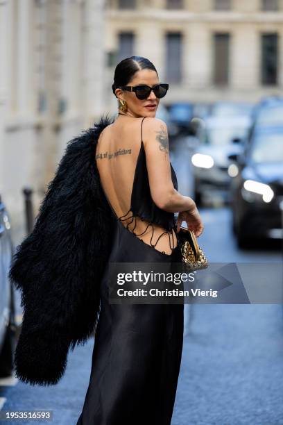 Gili Biegun wears golden bag, black cut out asymmetric dress, black faux fur coat outside Georges Hobeika during the Haute Couture Spring/Summer 2024...