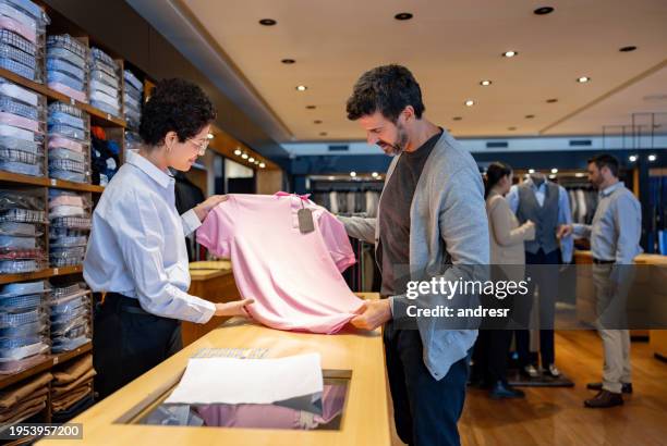 saleswoman selling a shirt to a man at a clothing store - garment stock pictures, royalty-free photos & images