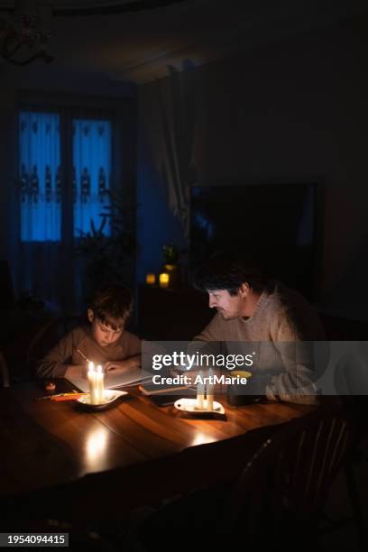 family sitting at home with candles during blackout. child is drawing, man is using power bank to charge his smartphone. energy crisis concept. - apagão imagens e fotografias de stock