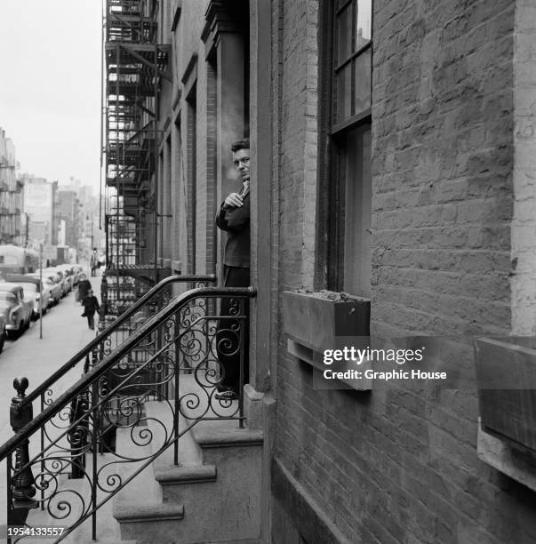 American actor Cliff Robertson, holding a lit cigarette partially obscured as he stands at the top of the stoop outside the Actors Studio on West...