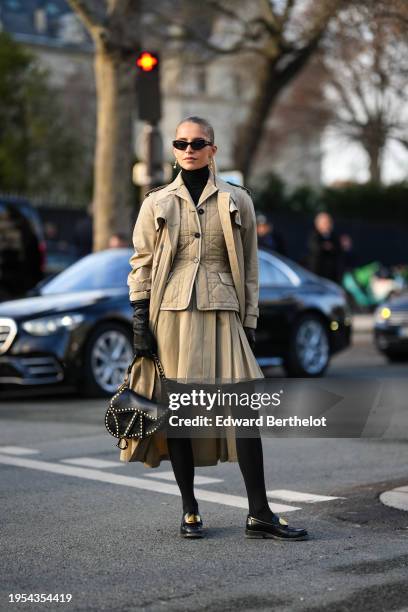 Caroline Daur wears earrings, a black turtleneck pullover, a beige long trench coat, black leather gloves, a leather Dior Saddle bag, a padded Dior...