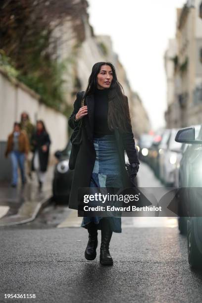Clemence Mouline wears a black turtleneck top, a black long winter coat, a blue patchwork denim skirt, black leather boots, outside Georges Hobeika,...