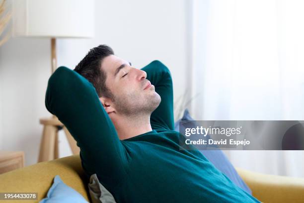 man relaxing on a sofa at home. - zurücklehnen stock-fotos und bilder