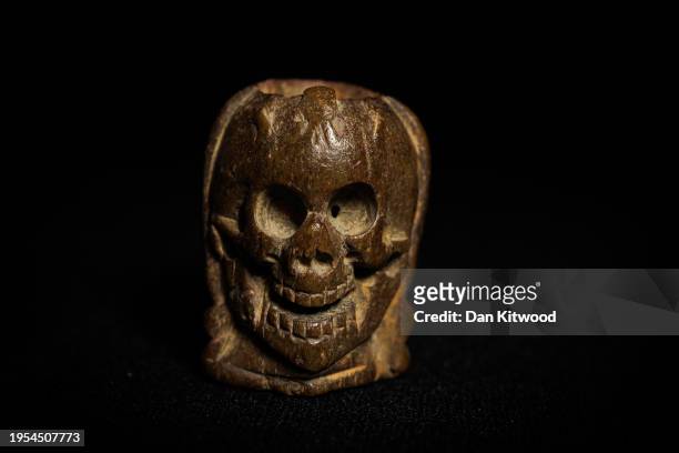 Carved bone rosary bead featuring a face on one side and a skull on the other that was discovered while mudlarking on the River Thames by Caroline...