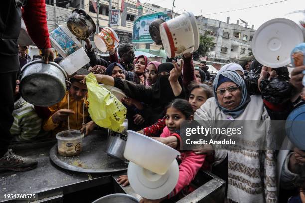 Palestinian people holding empty bowls try to reach out for food distributed by volunteers at donation point as Israeli attacks continue in Rafah,...