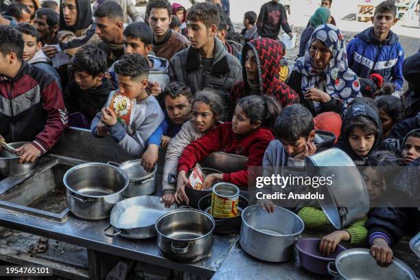 Palestinian people holding empty bowls try to reach out for food distributed by volunteers at donation point as Israeli attacks continue in Rafah,...