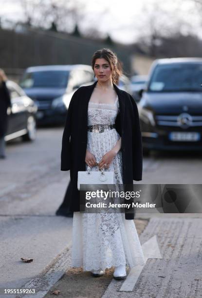 Amelie Zilber seen wearing white laced long dress, silver belt, white Dior handbag, black long wool jacket, white boots outside Christian Dior show...