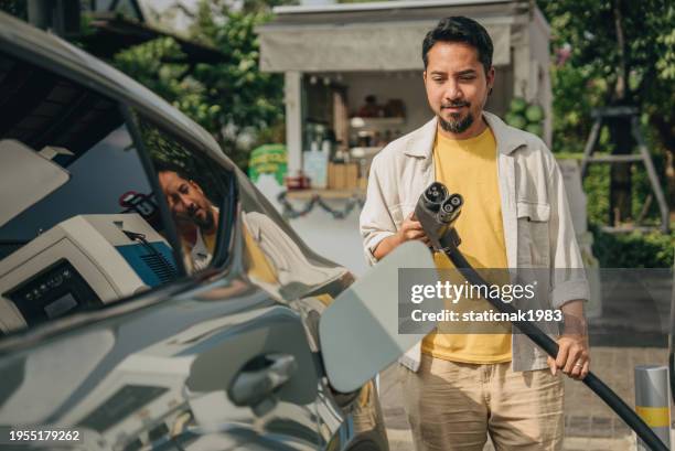asian man is opening the car hood to refuel his electric car at bangkok, thailand - fahrzeug mit hybrid antrieb stock-fotos und bilder