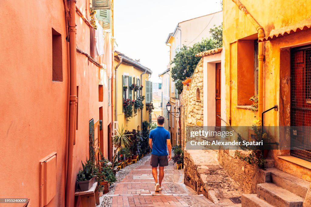 Rear view of a man exploring narrow alleys of Menton old town, French Riviera, France
