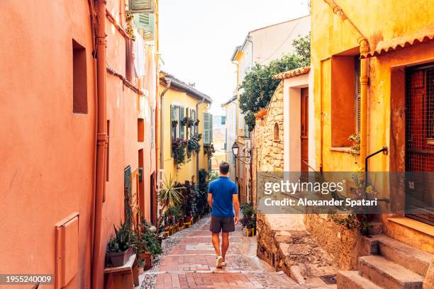 rear view of a man exploring narrow alleys of menton old town, french riviera, france - cote dazur stock pictures, royalty-free photos & images