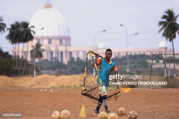 Young man carries a portable football goal during an amateur football match near the Notre Dame de la Paix Basilica in Yamoussoukro on January 25,...