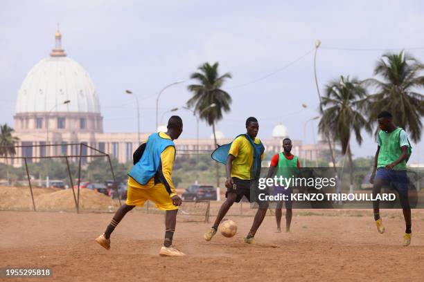 Young men play a football match near the Notre Dame de la Paix Basilica in Yamoussoukro on January 25, 2024.