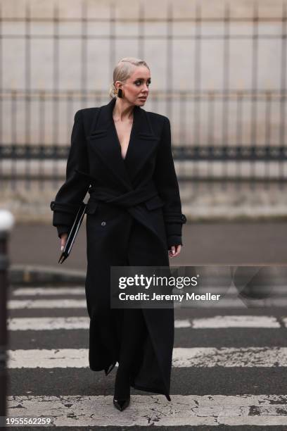 Sasha Ray seen wearing gold earrings, black elegant long wool coat, black wide leg long pants, black socks, black shiny varnished leather clutch bag...