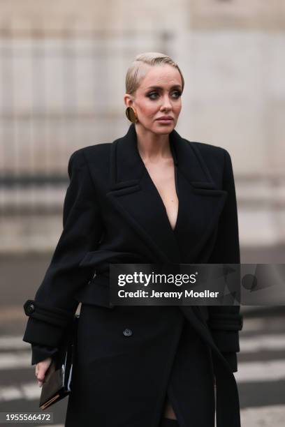 Sasha Ray seen wearing gold earrings, black elegant long wool coat, black wide leg long pants, black socks, black shiny varnished leather clutch bag,...