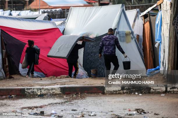 Displaced Palestinian uses a bucket to clear water from a tent drenched by heavy rain as children remove mattresses, at a makeshift camp set up by...