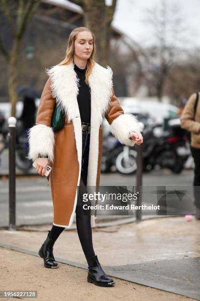 Guest wears a black top, a brown long aviator jacket with fluffy white lapel, black tights, black leather boots, outside Chanel, during the Haute...