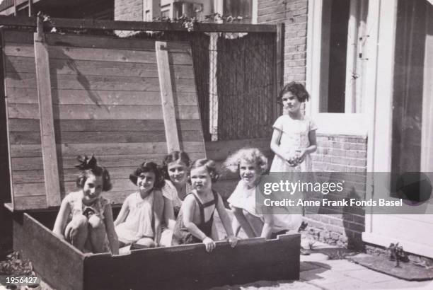 German Jewish refugee Anne Frank plays in a sandbox with friends. L to R: Hannelie Goslar, Anne Frank, Dolly Citroen, Hanna Toby, Barbara Ledermann,...