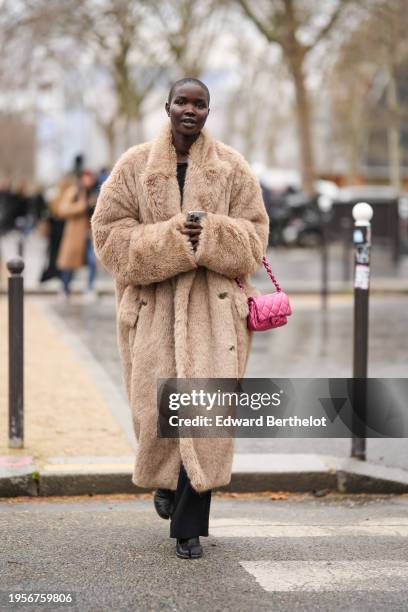 Model wears a brown / beige fluffy faux fur long winter coat, black pants, neon pink quilted Chanel bag, outside Chanel, during the Haute Couture...