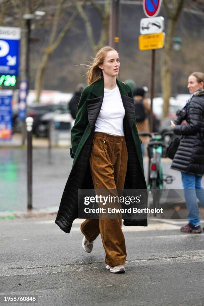 Model wears a white t-shirt, a green long coat with black quilted lapels, brown flared corduroy pants, sneakers shoes, outside Chanel, during the...