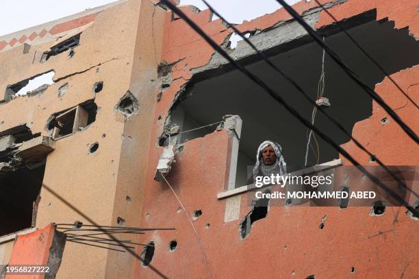 Man looks through the window of a building damaged by Israeli bombing, shows members of a family standing on a rooftop, in Rafah in the southern Gaza...