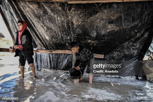 Child fills a bucket with rainwater after makeshift tents are flooded due to rain as Palestinians, who left their homes to protect themselves from...