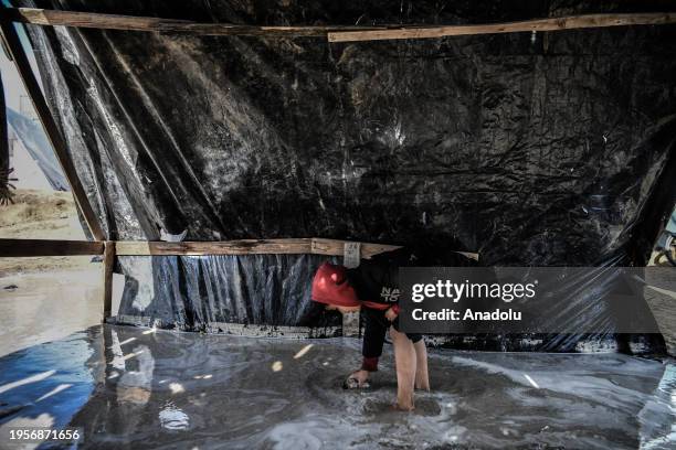 Child fills a bucket with rainwater after makeshift tents are flooded due to rain as Palestinians, who left their homes to protect themselves from...