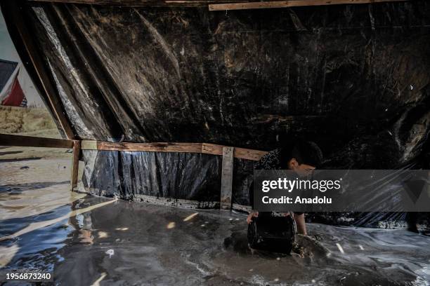 Child fills a bucket with rainwater after makeshift tents are flooded due to rain as Palestinians, who left their homes to protect themselves from...