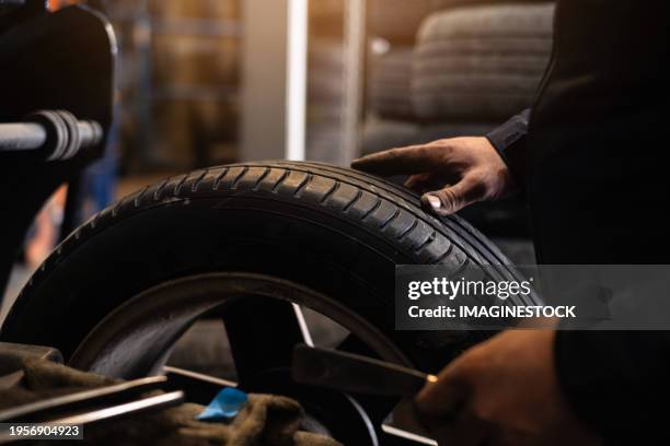 one young mechanic balancing a tire in auto repair shop. - neumático fotografías e imágenes de stock