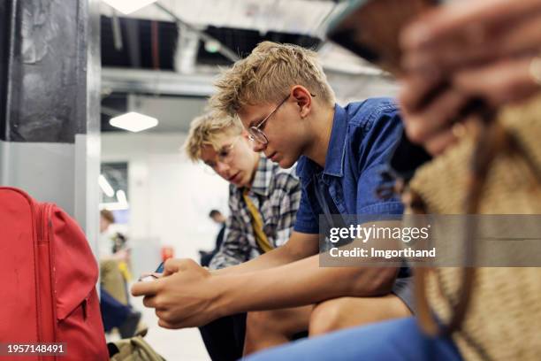 two teenagers waiting at the airport and playing with smart devices - recreational equipment stock pictures, royalty-free photos & images